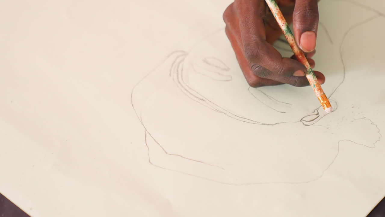 Black artist hand painting portrait sketch, closeup of dark skinned hand holding thin brush over pale paper, light graphite outline forming facial features, delicate dot and line marks, focused studio