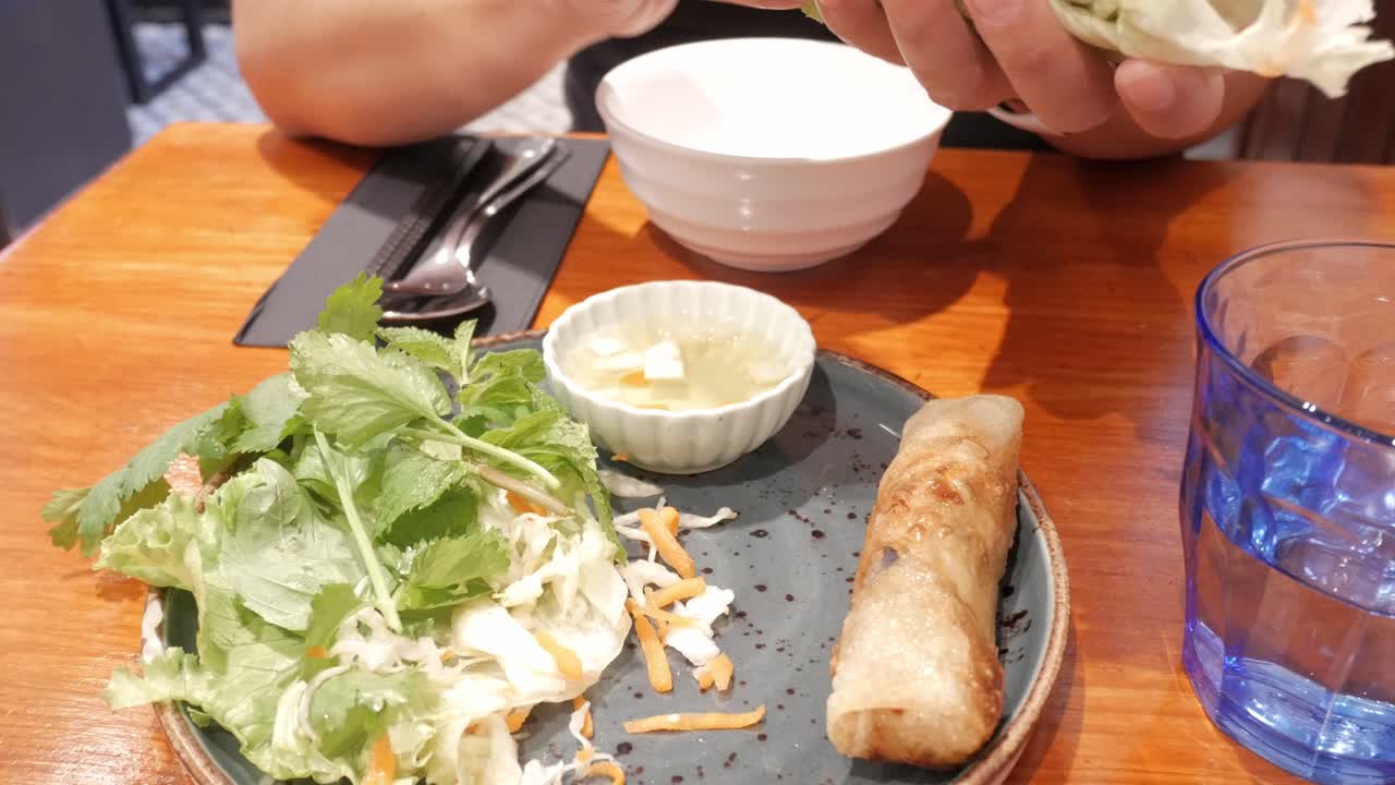 Popular Vietnamese spring rolls presented with garnish. Woman makes them ready and dips before eating them.