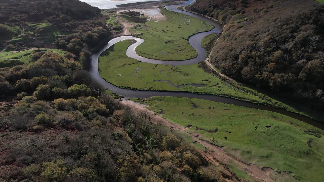 Aerial glide above Pennard Castle opening toward the green Three Cliffs Bay valley and meandering river in Wales