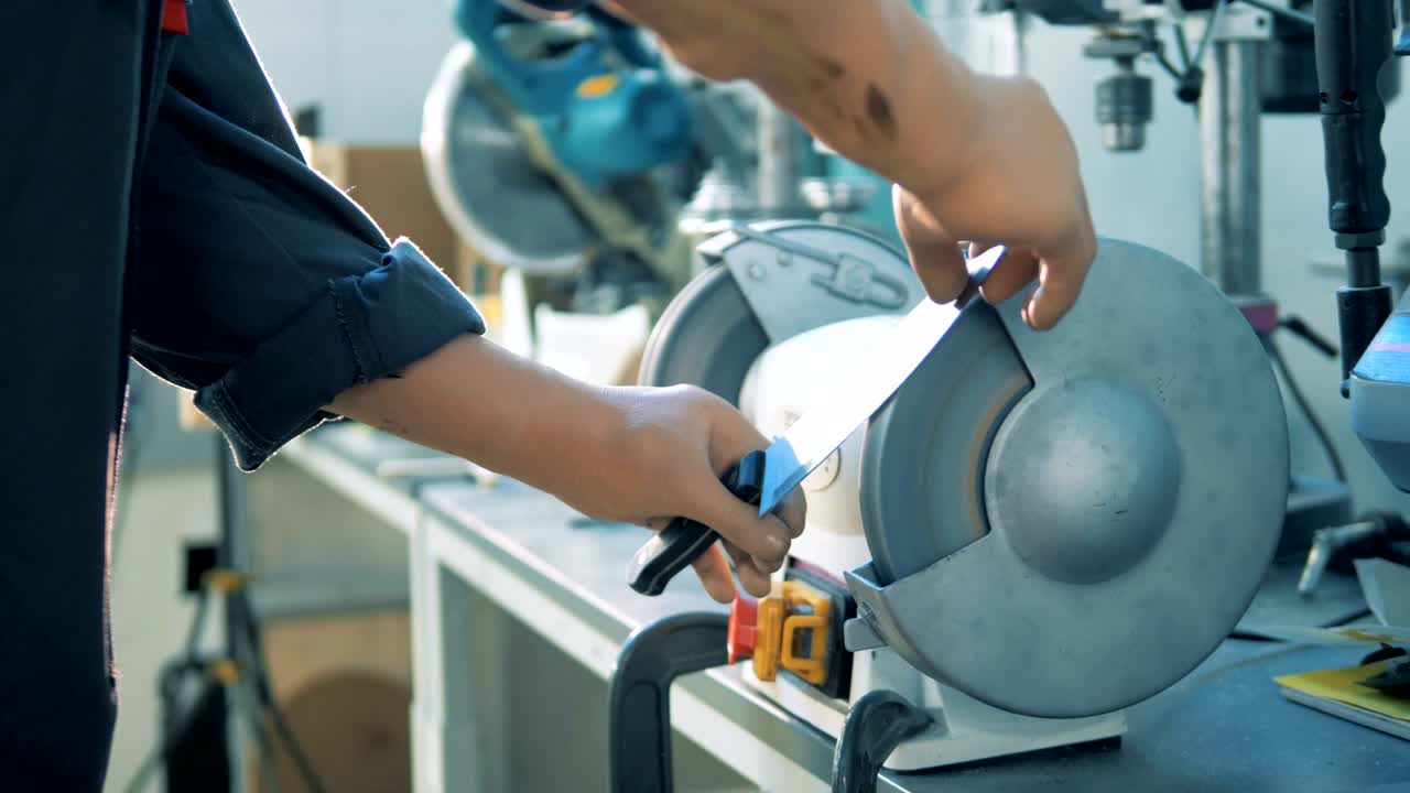 un especialista masculino con manos artificiales está afilando un cuchillo con un torno de metal