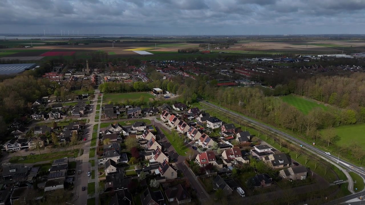 Drohnenaufnahme des niederländischen Dorfes Ens, Noordoostpolder, Flevoland, Niederlande. Überflug mit farbigen Feldern im Hintergrund.