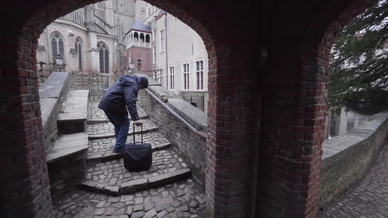 En anstrengt turist navigerer de brostensbelagte trin på Sankt Bonifacius-broen i Brugge, Belgien.