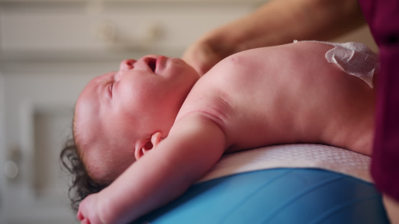 Baby placed on a stability ball while adults support the infant's body