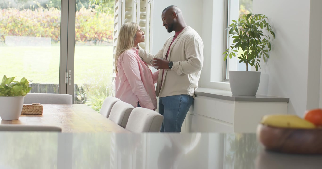 Couple at dining window, man placing hand on woman's shoulder while chatting at table, copy space