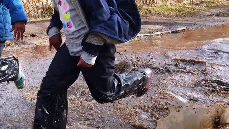 Children,-of-African-ethnicity,-running-and-splashing-in-a-large-puddle-of-water-for-fun