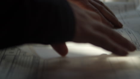 una franja de luz solar cae sobre las manos del diseñador, sus manos sostienen el papel con el diseño y un lápiz