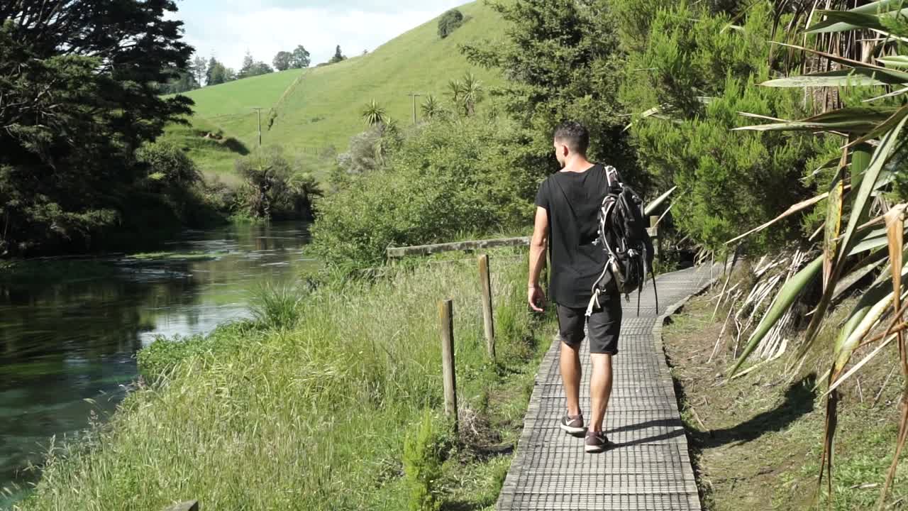 joven caucásico desde atrás camina a lo largo del río putaruru blue springng rodeado de exuberantes bosques nativos de nueva zelanda