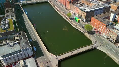 side-on, overhead aerial of the river liffey, the ha'penny bridge and dublin city centre in dublin, ireland on a bright and sunny day. filmed in 4k, 60fps and with rec709 color.