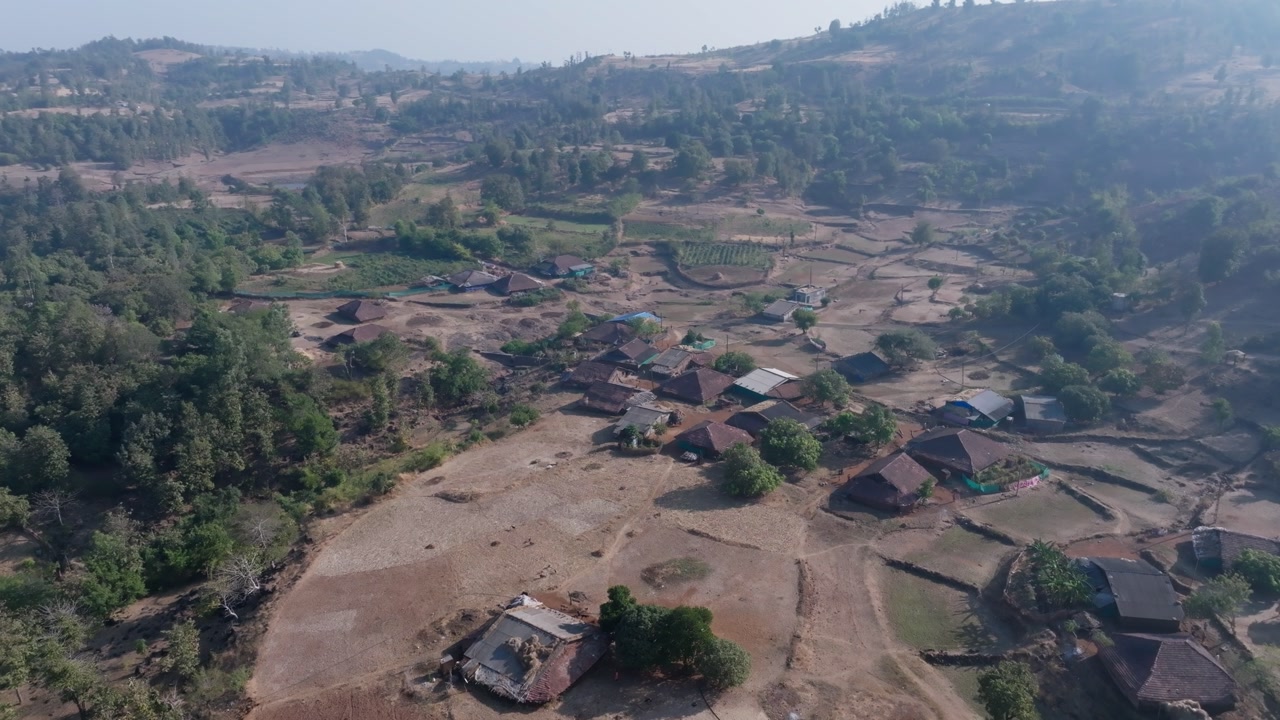 Smooth aerial drone footage slowly circling a rural village near in Gujarat. Traditional homes with terracotta roofs scattered across dry agricultural land.