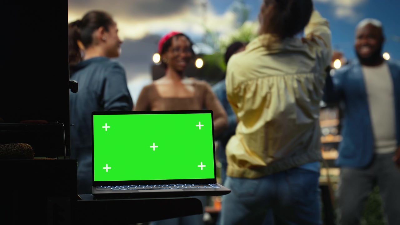 Editable green screen mockup on laptop at social gathering on rooftop