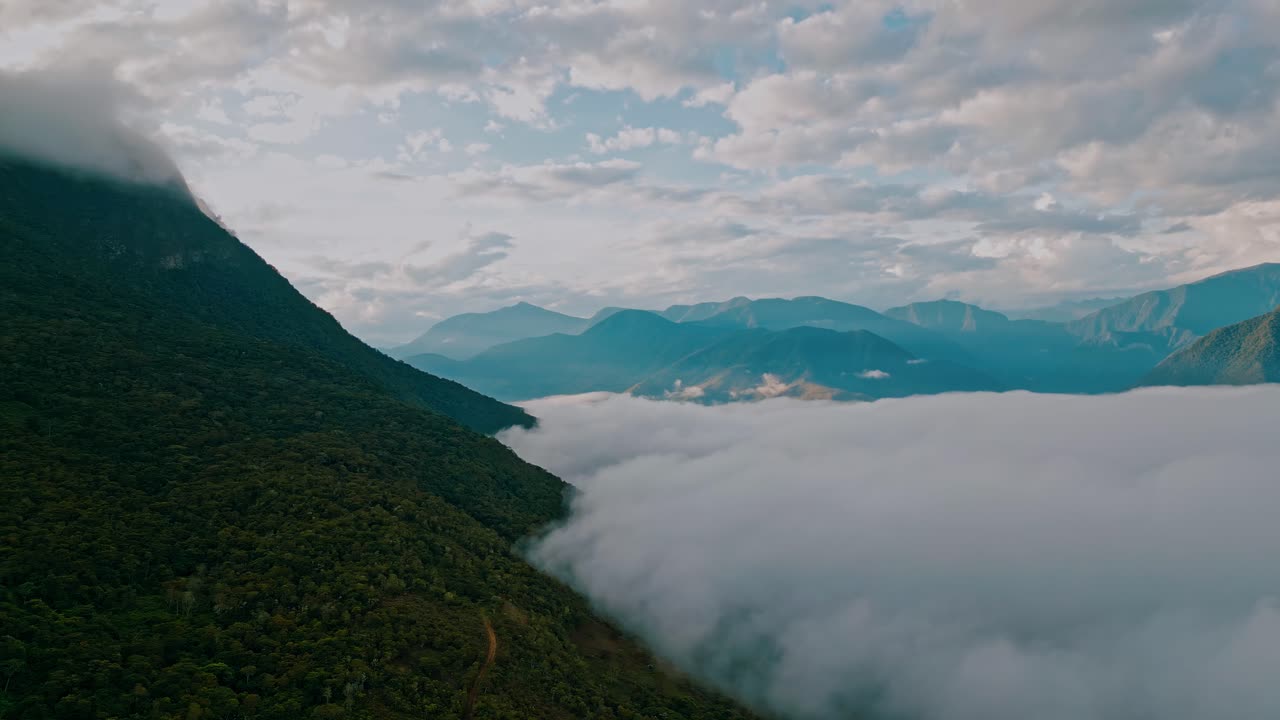 Behold the breathtaking Yungas cloud forest in this drone footage, as clouds veil a portion of the majestic mountain range, creating an alluring sense of mystery in this serene, lush landscape