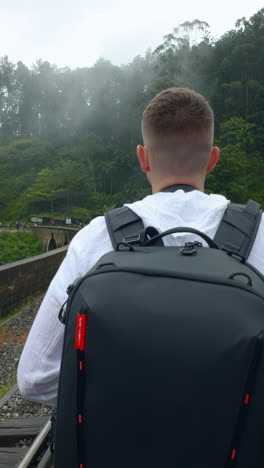 man with backpack walking on train tracks in a foggy forest