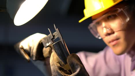 asian young engineer working and using tools measurement quality of metal parts. man wearing hardhat helmet safety with working workshop. concept of engineering, career, industry, manufacture, securit