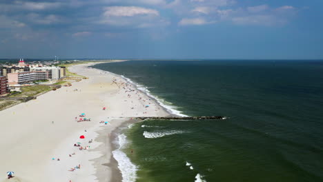 aerial-drone-pull-away-over-shoreline-on-the-left-in-Long-Beach-in-Long-Beach-New-York,-on-a-beautiful-sunny-day-with-clear-blue-skies-with-a-few-white-clouds