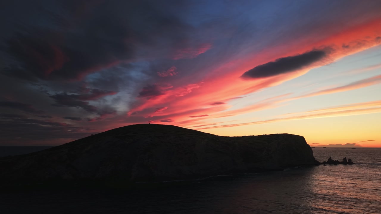 Drone moving along Illa des Bosc cliff in Ibiza with colorful sunset sky and ocean surrounding the island.