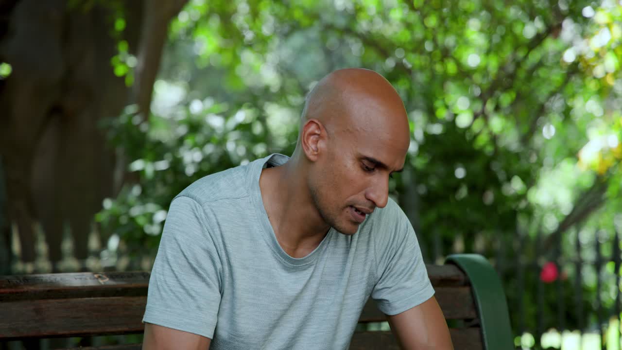 African American man sitting on bench in park, passersby causing glances, drinking to quench thirst