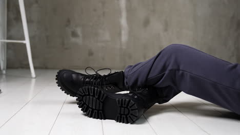 model in grey sportive pants sitting on the white floor in studio. female touching the tongues of black stylish army boots on her feet.