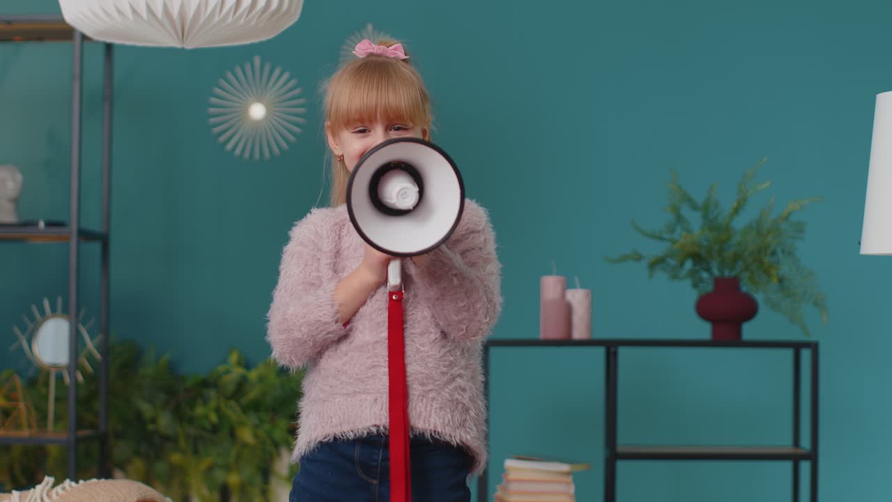 소녀 아이는 소파에 서서 집에서 혼자 큰 소리로 메가폰에 소리를 지르며 할인 판매를 발표합니다.