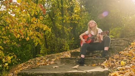 young blonde woman sits strums guitar autumn scene golden sunshine