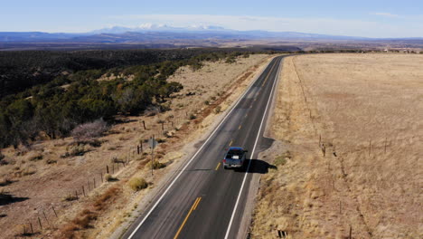 drone shot following a blue car running on a countryside highway in norwood, colorado