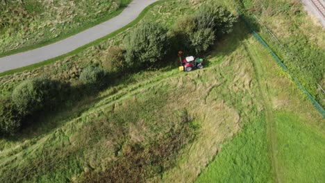 tractor in field trimming overgrown hedge and bush, aerial view overhead