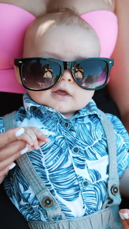 adorable baby boy lying on mom's belly face up. little child wearing mom's sunglasses looking cute. close up. vertical video