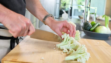 male chef slice cauliflower with the sharp knife on his cutting board