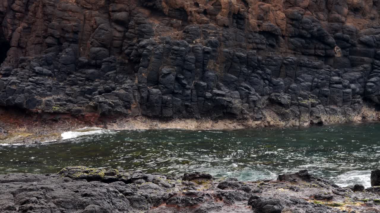 A mid shot of powerful waves crashing over jagged rocks along the shoreline, showcasing the raw energy of the ocean and dramatic coastal scenery.
