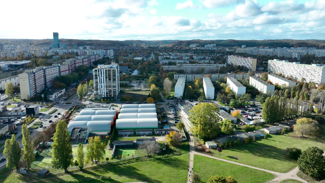 Wide drone shot of a dense urban district with high-rise blocks, green parks and a bright autumn landscape
