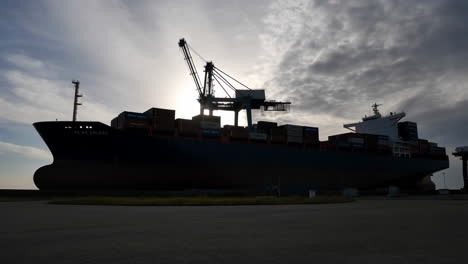 container ship and cranes silhouetted against a cloudy sky at port