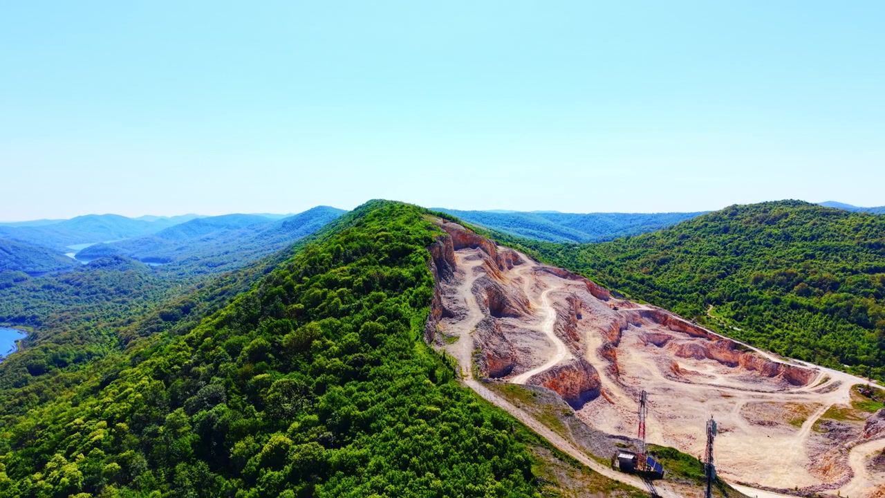 Sito minerario industriale su montagna, Bulgaria. Vista grandangolare di terreno scavato con sentieri tortuosi in cima a una vetta verdeggiante contro il cielo blu.