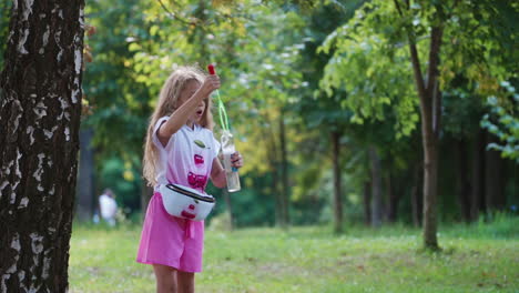 girl playing outdoor. happy little girl blowing soap bubbles in park