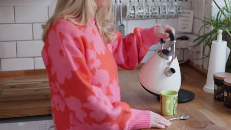 woman pouring water from kettle into a mug in kitchen