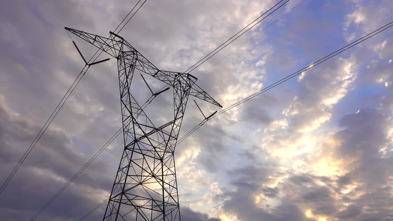 Large, looming electrical transmission tower with dramatic blue and cloudy sky behind