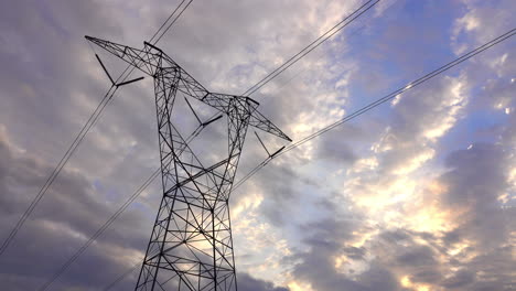 Large,-looming-electrical-transmission-tower-with-dramatic-blue-and-cloudy-sky-behind