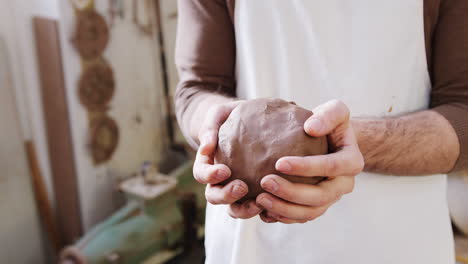 Primer-Plano-De-Un-Alfarero-Masculino-Con-Delantal-Sosteniendo-Un-Trozo-De-Arcilla-En-Un-Estudio-De-Cerámica