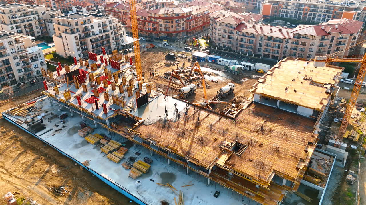Draufsicht auf den Betonierprozess auf einer Baustelle. Arbeiter gießen Beton für eine Fundamentplatte, unterstützt von zwei Betonpumpen und Kränen.