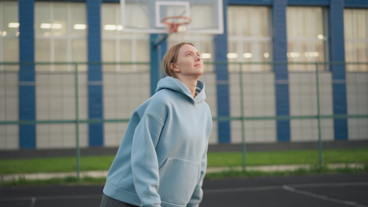 Lady in blue hoodie serves volleyball, watching it as it leaves her hand, outdoor volleyball practice session with focus on serve action and athletic technique
