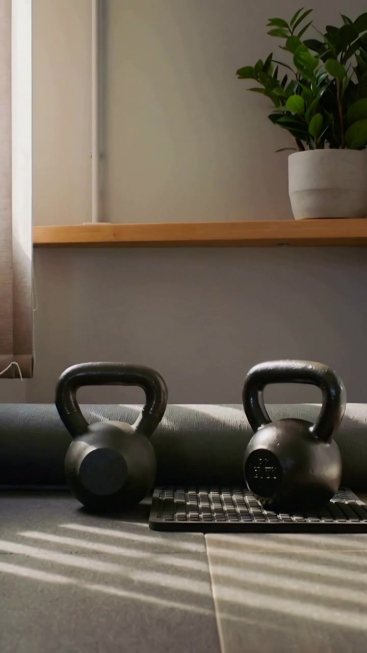 Vertical video: Pulling back cam showing two kettlebells in home gym with foam roller and sun rays