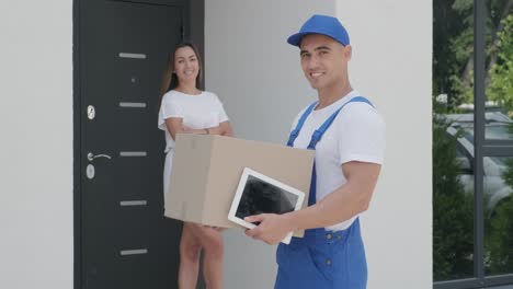 beautiful woman meets a delivery man with parcel box and tablet beside her home. concept of courier, home delivery, online shopping