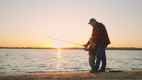 happy granddad and little boy are fishing in sunset time old fisher and grandson are catching fish