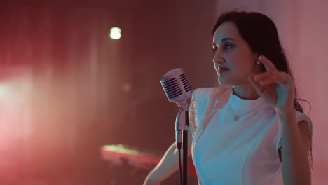 a singer stands in front of a vintage microphone, moving her hands and body passionately. the side-angle shot captures the dynamic energy and expressive performance in a warmly lit