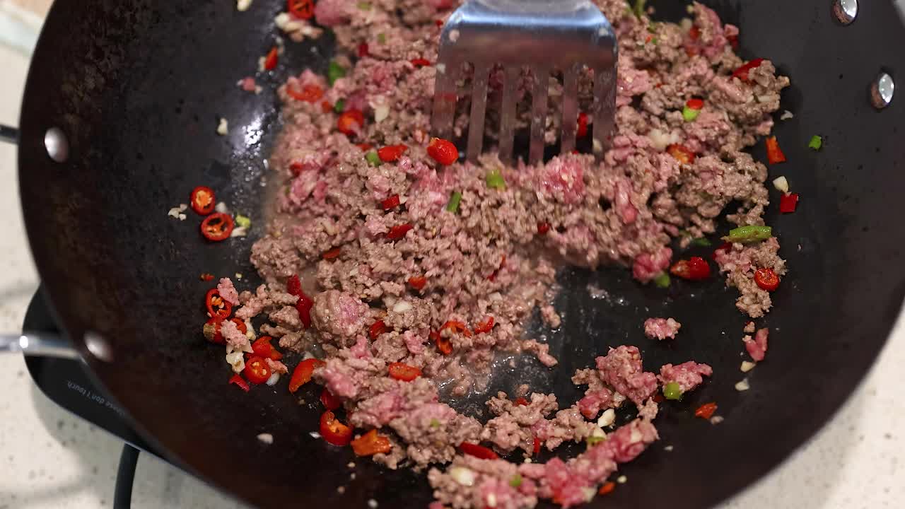 Ground beef and vegetables are stir-fried in a wok, showcasing a vibrant cooking process with a spatula