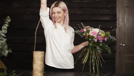 A-young-smiling-woman-in-white-playfully-unwinds-the-twine-,-cuts-off-a-piece-and-tightens-stems-of-flowers