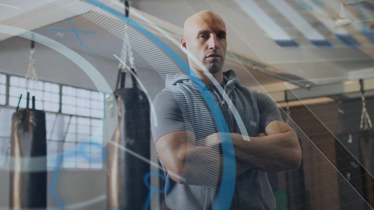 Vertical video: Posing man in hoodie at gym punch bags, overlays sweeping causing cam moving closer