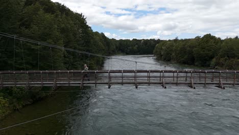 hiking woman walking on hanging wooden footbridge over flowing river