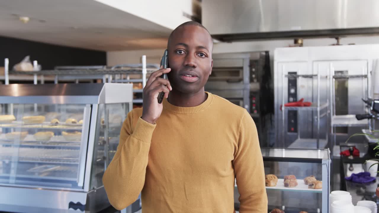 Portrait of happy african american man talking on smartphone in bakery in slow motion