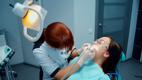 medical procedure in dentistry. young woman in protective glasses in dental chair. female stomatologist cures patient's teeth in clinic.