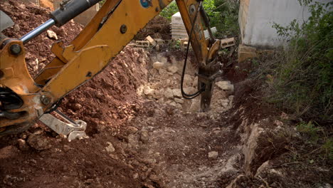 Slow-motion-of-a-backhoe-loader-with-an-hydraulic-hammer-attached-drilling-breaking-rocks-in-a-hole-for-a-pool