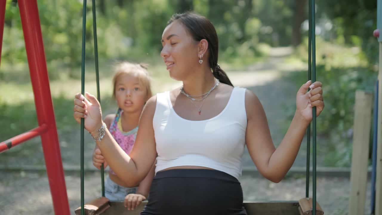 임신 한 어머니 와 딸 이 야외 에서 스 에서 놀고 있다